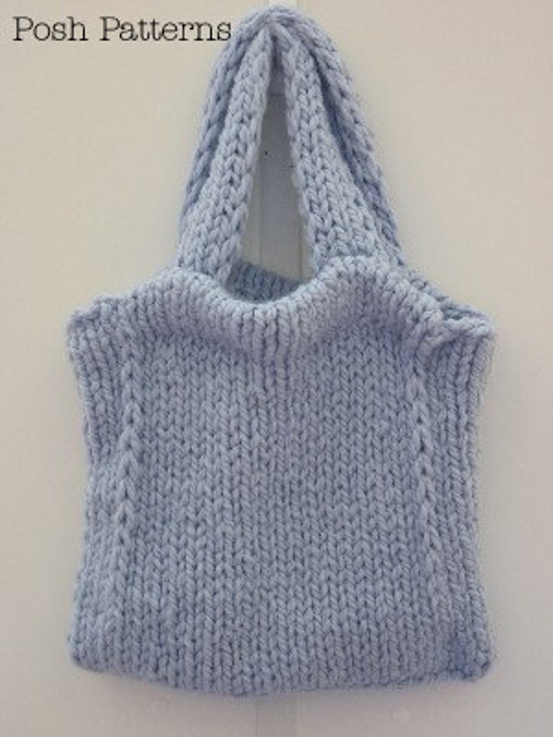 K&ouml;nnte beinhalten: Eine hellblaue gestrickte Einkaufstasche mit einem breiten, flachen Boden und zwei dicken Henkeln. Die Tasche ist mit einem einfachen Stichmuster gearbeitet und hat eine leicht strukturierte Oberfl&auml;che.