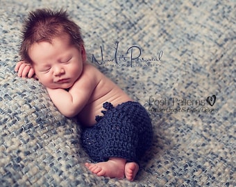 Könnte beinhalten: Ein neugeborenes Baby, das eine blaue gestrickte Windelhülle trägt, schläft auf einer strukturierten blauen Decke. Das Baby liegt auf der Seite, der Kopf ruht auf dem Arm. Das Bild enthält den Text "Now It's Personal Photography" und "Posh Patterns Modern Crochet & Knitting Designs".