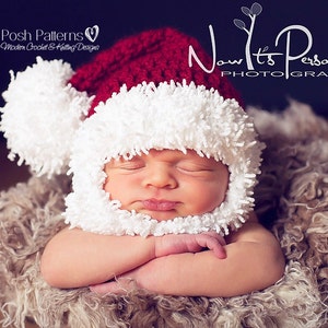 Puede incluir: Un beb&eacute; reci&eacute;n nacido con un gorro de Pap&aacute; Noel de crochet blanco y rojo con un pomp&oacute;n esponjoso. El beb&eacute; est&aacute; durmiendo con los brazos cruzados y est&aacute; acostado sobre una superficie esponjosa marr&oacute;n.