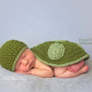 May include: A newborn baby wearing a green crocheted turtle costume with a matching hat. The costume features a green and light green shell with a textured design.