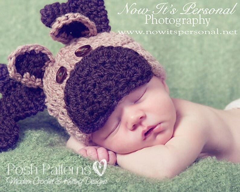 May include: A newborn baby wearing a brown and beige crocheted dog hat with floppy ears. The baby is sleeping on a green blanket. The hat has brown buttons for eyes and a brown nose.