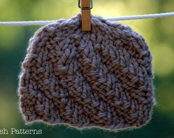 Puede incluir: Un gorro de punto marrón colgado de una cuerda para tender la ropa con una pinza de madera. El gorro tiene un patrón texturizado y está hecho de un hilo suave y peludo.