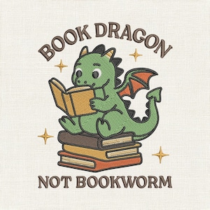Könnte beinhalten: Gesticktes Design mit einem grünen Drachen, der ein Buch auf einem Stapel von Büchern liest. Der Text lautet "BOOK DRAGON NOT BOOKWORM" in braunen Buchstaben, mit Sternakzenten. Der Drache hat orangefarbene Flügel und einen freundlichen Ausdruck.