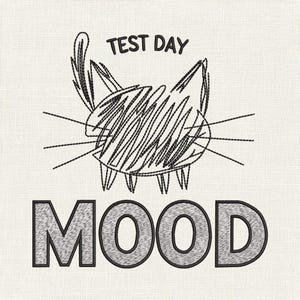 Puede incluir: Diseño bordado con una ilustración de gato y las palabras "TEST DAY" y "MOOD". El gato está dibujado con líneas negras y relleno con líneas garabateadas. El texto está en una fuente en negrita y en bloque, también en negro.