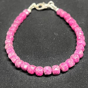 May include: A pink gemstone bracelet with a silver clasp. The bracelet is made of small, faceted, pink gemstones strung together. The clasp is a simple hook and eye design.