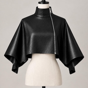 Peut inclure: Une veste cape courte en similicuir noir dot&eacute;e d'un col montant et d'une fermeture &eacute;clair asym&eacute;trique en m&eacute;tal argent&eacute;. Le v&ecirc;tement pr&eacute;sente des manches larges et &eacute;vas&eacute;es qui tombent des &eacute;paules, cr&eacute;ant une silhouette structur&eacute;e.