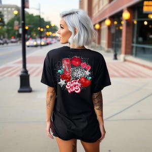 May include: Black t-shirt with a graphic print of a red can, a disco ball, cherries, and lips. The text "Good Vibes" is printed in red and white.