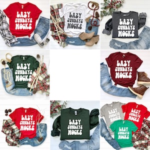 May include: Nine different t-shirts featuring the text "Lazy Sundays MOGKS" in a white, retro font. The shirts are displayed against a white backdrop with various props, including jeans, plaid scarves, and pine cones.