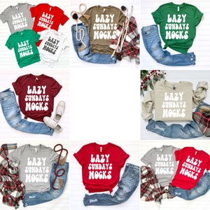 May include: A collection of t-shirts in various colours featuring the text "Lazy Sundays MOGKS" in a white retro font. The shirts are displayed on a white background with jeans and other accessories.