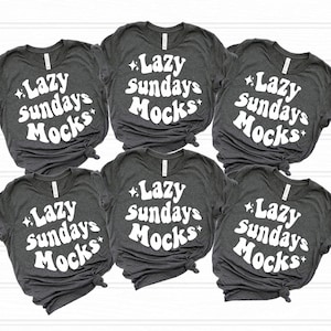 May include: Six gray t-shirts with the text "Lazy Sundays Mocks" printed in white on the front. The text is in a retro font style.