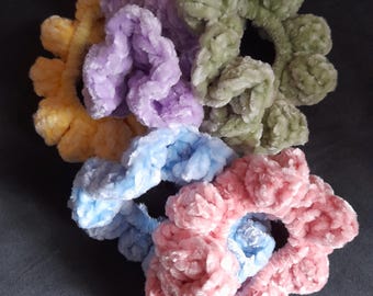 May include: A collection of six plush scrunchies in various pastel colors. The scrunchies are in shades of yellow, lavender, green, blue, and pink. The scrunchies are made of a soft, velvety material and are arranged in a circular pattern.