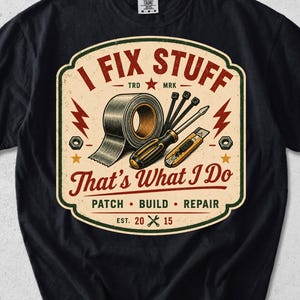 May include: A black short-sleeve t-shirt featuring a graphic print with the text I FIX STUFF That's What I Do PATCH BUILD REPAIR EST 2015. The design includes illustrations of a roll of duct tape, a screwdriver, a utility knife, and zip ties.