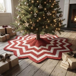 May include: A star-shaped crochet Christmas tree skirt featuring a repeating chevron pattern in alternating bands of deep red and cream white yarn. The skirt is positioned around the base of a decorated evergreen tree with warm fairy lights.