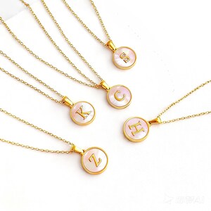 Peut inclure: Colliers dorés avec des pendentifs ronds, chacun portant une lettre différente : S, C, K, H et Z. Les pendentifs ont un effet nacré et sont suspendus à de fines chaînes. Un bijou élégant et personnalisé.