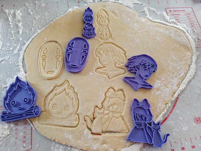 May include: A sheet of dough with various purple cookie cutters in the shapes of characters from a popular animated film. The cut dough shows the impressions of the characters. The scene is on a white surface.