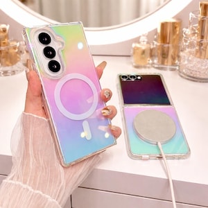 Könnte beinhalten: Eine transparente Handyhülle mit Regenbogen-Farbverlauf und kreisförmiger Magnetbefestigung. Die Hülle wird neben einem zusammengeklappten Handy mit passendem Farbverlauf und einem silbernen magnetischen Ladepad gehalten.