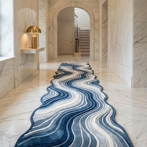 May include: A long, narrow runner rug featuring a wavy, organic shape with a layered pattern of blue, navy, and white stripes. The rug has a textured, tufted surface and follows a fluid, undulating design that stretches across the floor.