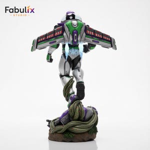 May include: A detailed figurine of Buzz Lightyear in a dynamic pose, viewed from the back. The figure features a silver, green, and purple color scheme with outstretched wings. The base is a detailed, earthy design with vines.
