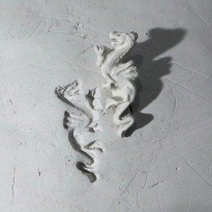 May include: Two white ceramic dragon figurines, one on top of the other, with intricate details and a textured surface.