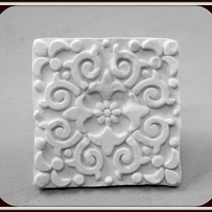 Pode incluir: Azulejo de cerâmica branco com um design em relevo intrincado de padrões florais em espiral.