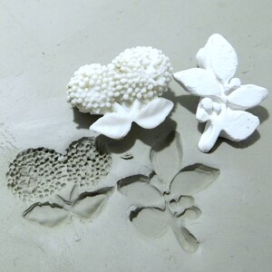 Pode incluir: Moldes de cerâmica branca de flores e folhas sobre uma superfície cinza. Os moldes são usados para criar impressões em argila.