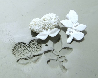 May include: White ceramic molds of flowers and leaves on a gray surface. The molds are used to create impressions in clay.