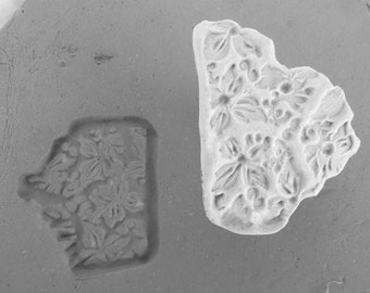 May include: A gray silicone mold with a floral design and a matching cast piece. The cast piece is a light color, showing the detailed floral pattern of flowers and leaves. The mold is rectangular with rounded edges.