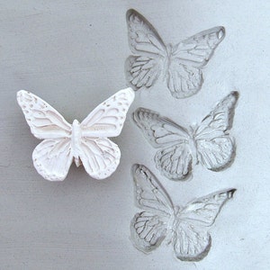May include: A white butterfly mold with three butterfly impressions. The mold is made of silicone and is used to create decorative butterflies.