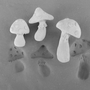 May include: Five white ceramic mushrooms of varying sizes and shapes. The mushrooms are arranged on a light gray surface.