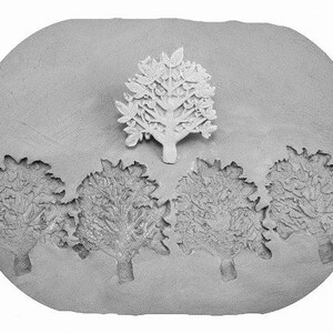 May include: A gray clay mold with five tree designs. The center tree is raised and the four surrounding trees are indented.