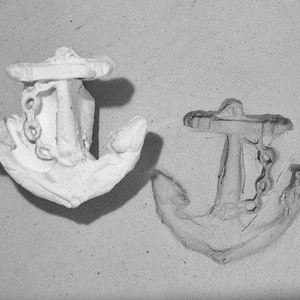 May include: Two white ceramic anchors, one with a chain detail, are shown on a light gray surface.