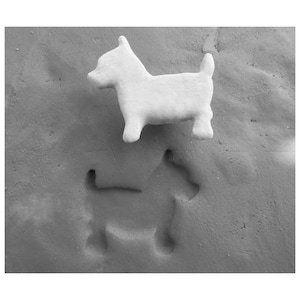 May include: A white ceramic dog figurine on a gray textured surface. A shadow of a dog is imprinted in the surface.