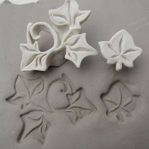 May include: A set of four white ceramic ivy leaf stamps. The stamps are used to create impressions in clay or other soft materials.