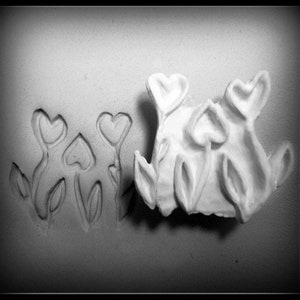 May include: A white ceramic wall decor with a design of stylized flowers. The flowers are shaped like hearts and have a simple, minimalist design.