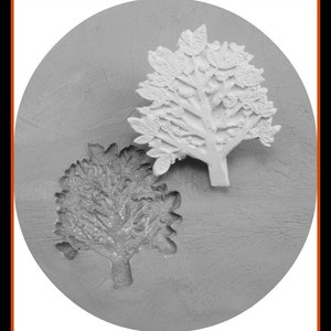 May include: A close-up of a grey silicone mould with two tree designs. The mould is circular and has a textured surface. One tree design is detailed with leaves and the other is more abstract.