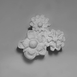 May include: A white ceramic ornament with a cluster of three stylized flowers. Each flower has a raised center and intricate details.