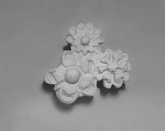 May include: A white ceramic ornament with a cluster of three stylized flowers. Each flower has a raised center and intricate details.