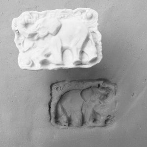 May include: A white, detailed, three-dimensional elephant sculpture in a rectangular frame. The sculpture is shown next to a mould of the sculpture.