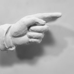 Pode incluir: Uma escultura de mão de gesso branco apontando para a direita.