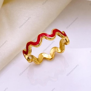 Puede incluir: Un anillo de tono dorado con un diseño de banda ondulada o en zigzag continua. La mitad superior de la estructura ondulada está rellena con un esmalte rojo vibrante, mientras que la mitad inferior y los lados de la banda mantienen un tono dorado pulido.