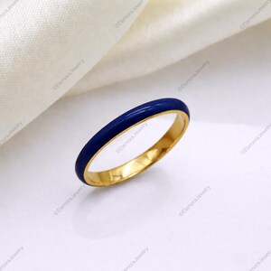 Könnte beinhalten: Ein goldener Ring mit einem leuchtend blauen Emailleband. Der Ring hat eine polierte Oberfläche und wird vor einem weißen Hintergrund präsentiert. Der Ring ist ein Schmuckstück.