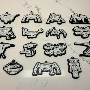 May include: A collection of black and white pendants with various futuristic designs. The pendants feature detailed illustrations of spacecraft, robots, and other sci-fi elements. Each pendant has a small loop for hanging.