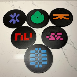May include: Six black round coasters with colorful geometric designs. The designs include purple, green, orange, red, pink, and blue shapes. The coasters are arranged in a circular pattern.