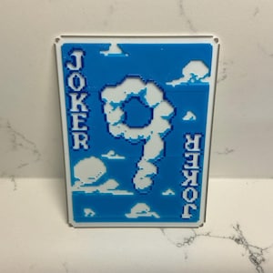 May include: A rectangular metal sign featuring a blue background with white pixelated clouds and the word "JOKER" in white block letters on the sides. The number "9" is formed by a cloud shape in the center.
