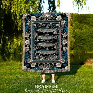 Puede incluir: Una manta negra con un diseño de peces. La manta presenta cuatro peces en fila, con un borde floral en blanco y turquesa. El texto "BRAINSUBI Original Fine Art Throws" está en la parte inferior.