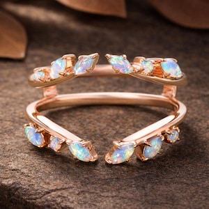 Op de afbeelding: Roségouden ring met een uniek ontwerp. De ring heeft meerdere opaal edelstenen in een bladvormige opstelling. De opalen hebben een mix van blauwe, groene en witte kleuren. De ring staat tegen een neutrale achtergrond.