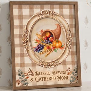 Puede incluir: Un cuadro rectangular con marco que presenta un fondo de cuadros beige y blanco. Un marco ovalado ornamentado rodea un cuerno de la abundancia lleno de manzanas, uvas y una calabaza. El texto dice Blessed Harvest & Gathered Home.