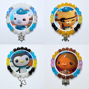 May include: Four circular beaded bracelets featuring Octonauts character inserts. The top left has a white polar bear, top right an orange cat with an eyepatch, bottom left a penguin, and bottom right a brown creature with a camera charm.
