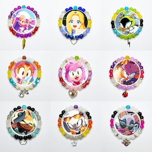 May include: A collection of nine circular beaded bracelets, each featuring a central character illustration from the Sonic the Hedgehog series. The bracelets are crafted with colorful beads and include various metal charms like a feather, heart, and star.