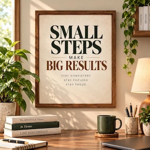 May include: A framed wall art print with a dark wood frame featuring the text SMALL STEPS MAKE BIG RESULTS in dark green and brown, followed by the smaller text STAY CONSISTENT, STAY FOCUSED, and STAY PROUD on a light beige background.
